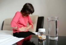 Mujer que sufre de dolor en el abdomen. Botella de pastillas y vaso de agua en una mesa / laxantes
