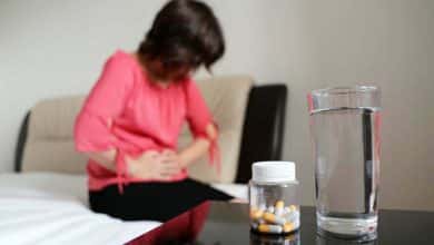 Mujer que sufre de dolor en el abdomen. Botella de pastillas y vaso de agua en una mesa / laxantes