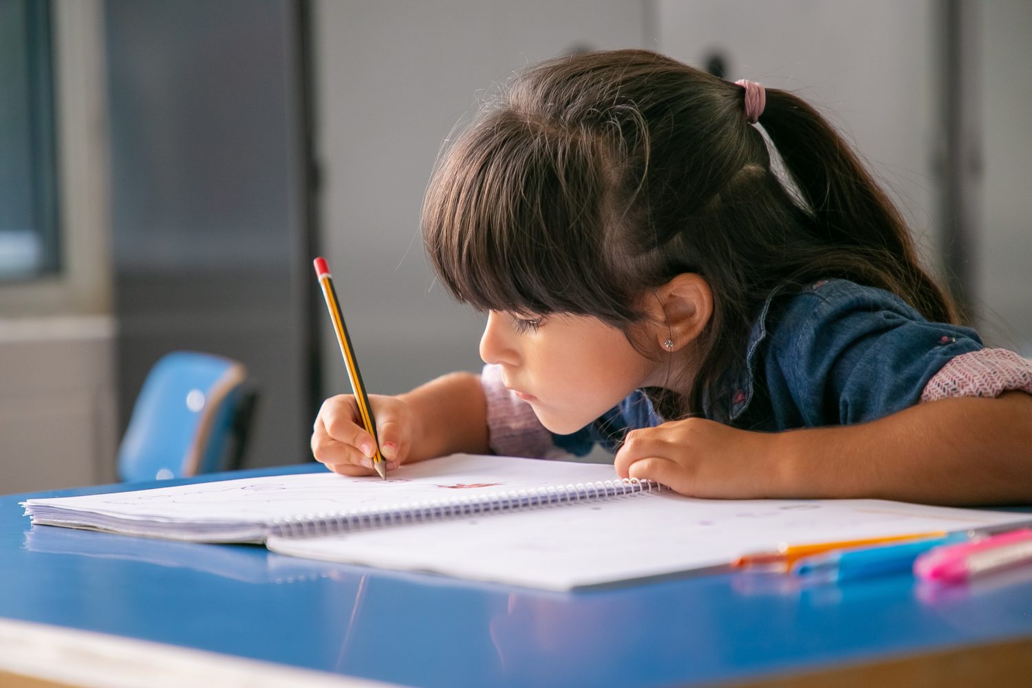 chica latina de pelo enfocada sentada en el pupitre de la escuela y dibujando estudiar con disciplina