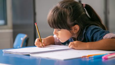 chica latina de pelo enfocada sentada en el pupitre de la escuela y dibujando estudiar con disciplina