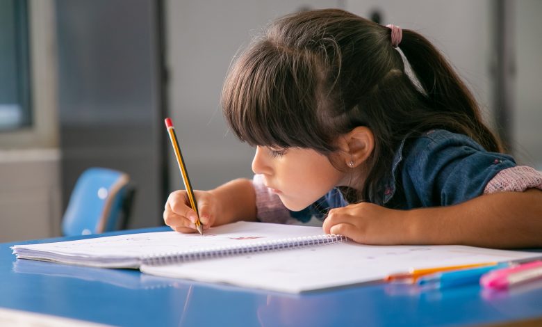 chica latina de pelo enfocada sentada en el pupitre de la escuela y dibujando estudiar con disciplina
