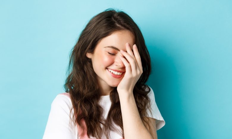 bella joven que se r&iacute;e y ruboriza, cubriendo la cara / eritrofobia