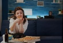 mujer joven comiendo pizza mientras mira la televisión