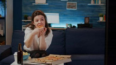 mujer joven comiendo pizza mientras mira la televisi&oacute;n