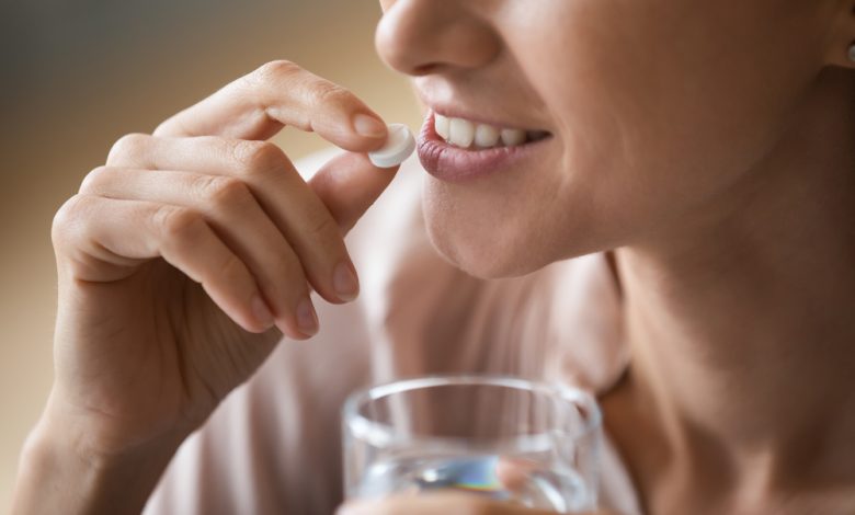 mujer atractiva sonriente sosteniendo una pastilla blanca redonda y un vaso de agua / alimentos