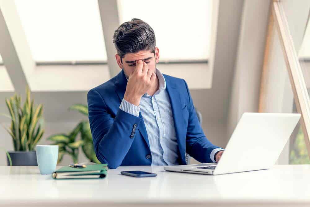 hombre de negocios exhausto con las manos en la frente sentado en la oficina / gafas para usar el computador