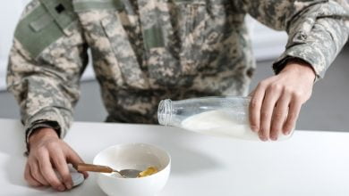 vista recortada del militar vertiendo leche en un taz&oacute;n con copos de ma&iacute;z / dieta militar