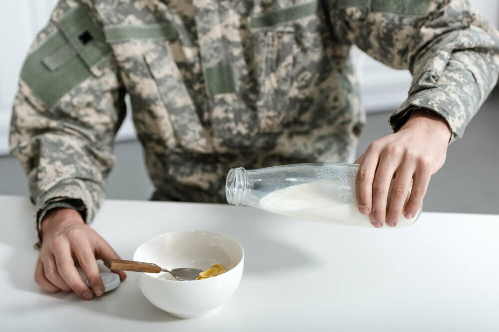 vista recortada del militar vertiendo leche en un tazón con copos de maíz / dieta militar