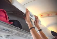 mano de una mujer pasajera del avión sosteniendo la cubierta del casillero superior para mantenerla cerrada, para mantener los equipajes a salvo durante el vuelo / equipaje de mano