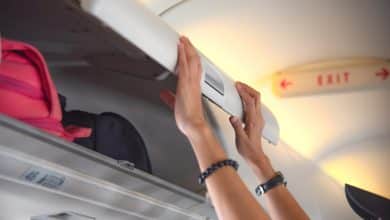 mano de una mujer pasajera del avi&oacute;n sosteniendo la cubierta del casillero superior para mantenerla cerrada, para mantener los equipajes a salvo durante el vuelo / equipaje de mano