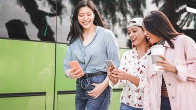 Felices amigos asiáticos que usan smartphones en la estación de autobuses / mantenerte delgado