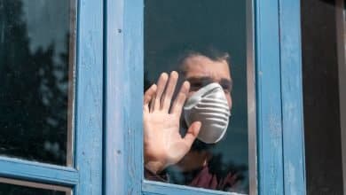 Hombre enfermo mirando por la ventana y usando m&aacute;scara de protecci&oacute;n / pandemia