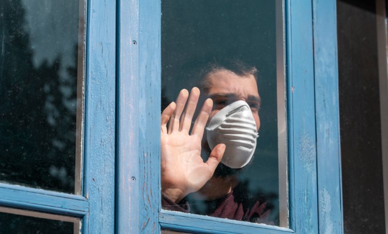Hombre enfermo mirando por la ventana y usando máscara de protección / pandemia