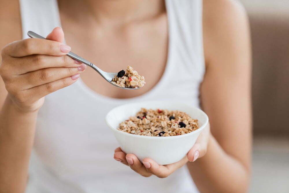 Imagen recortada de una mujer sosteniendo un tazón con granola o harina de avena casera / desayuno