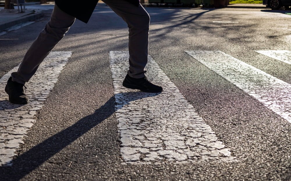 hombre tratando de no pisar las l&iacute;neas negras de un paso peatonal / man&iacute;as