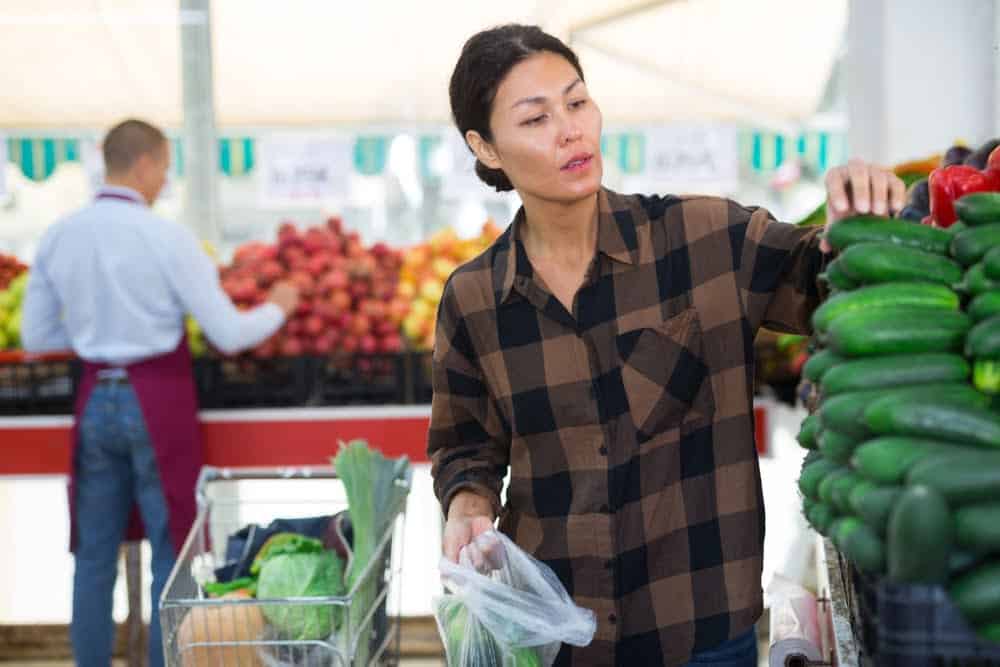 Mujer asi&aacute;tica eligiendo pepinos en verdulera / pepino